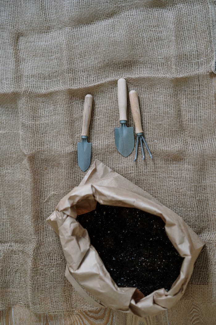 Flatlay of gardening tools and soil on burlap, perfect for agriculture themes.